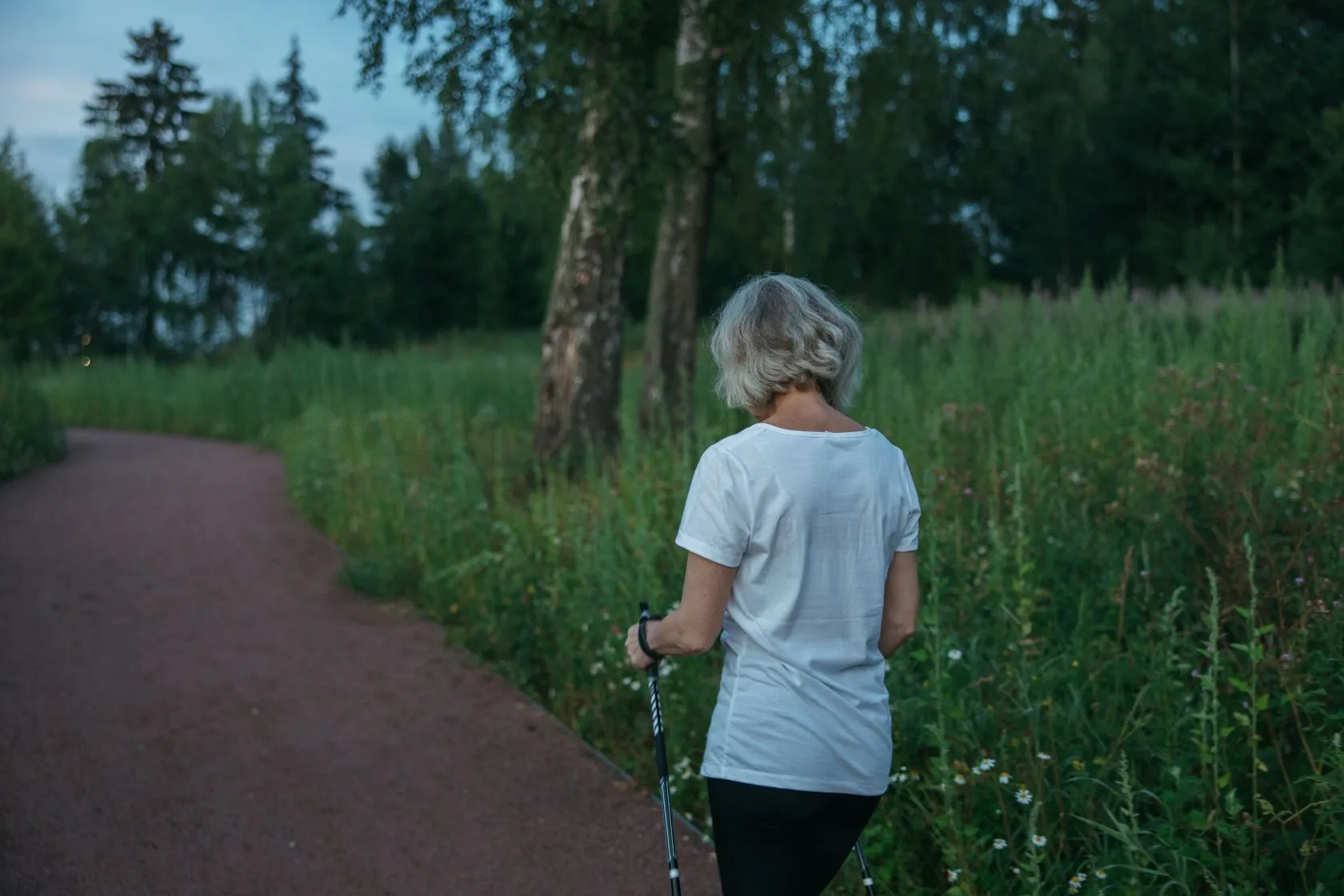 An older woman out walking on a tree-lined path.
